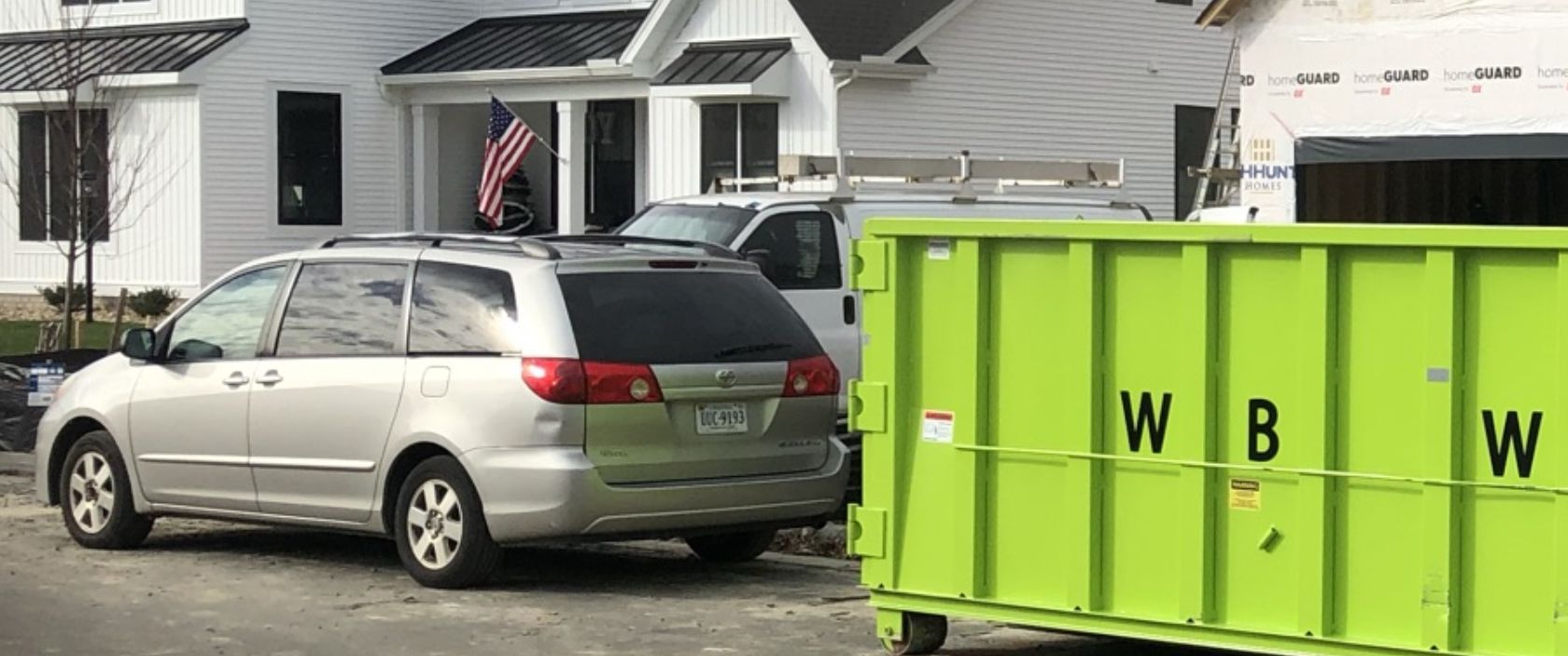 green dumpster behind minivan.