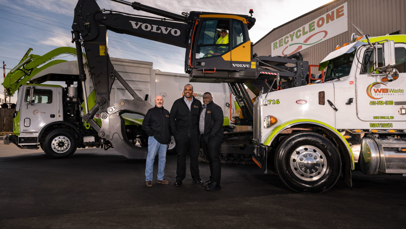 three men standing in front of trucks and heavy equipment.
