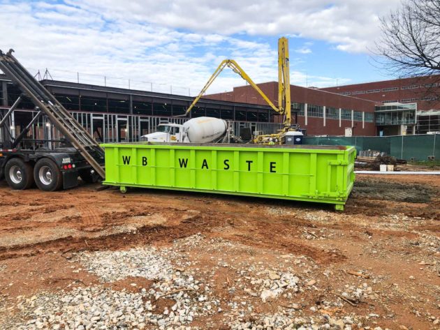 green commercial dumpster that says wb waste at a construction site.