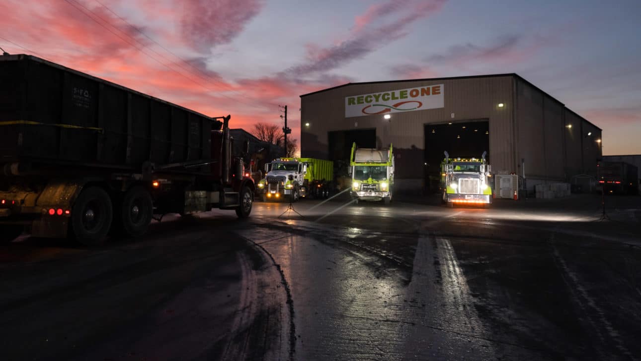 trucks coming out of garage under pink and blue sky at dusk.