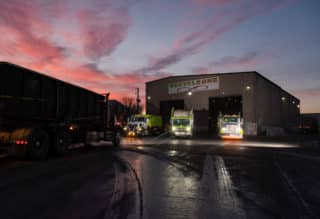 trucks coming out of garage under pink and blue sky at dusk.