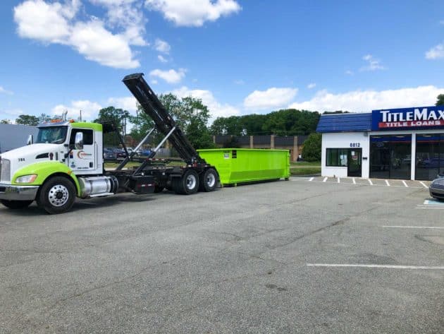 roll of dumpster being loaded onto truck at loan business parking lot.