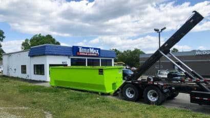 commercial dumpster being loaded onto a truck bed.