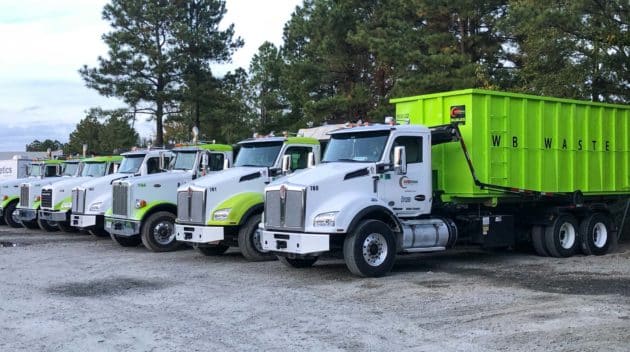 row of trucks with green dumpsters.